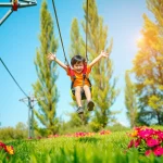 Experience the thrill of the GARDEN ZIP WIRE KIT with a child soaring above vibrant flowers and greenery.